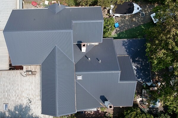 An aerial view of a single-storey house with a gray roof, nestled among trees.